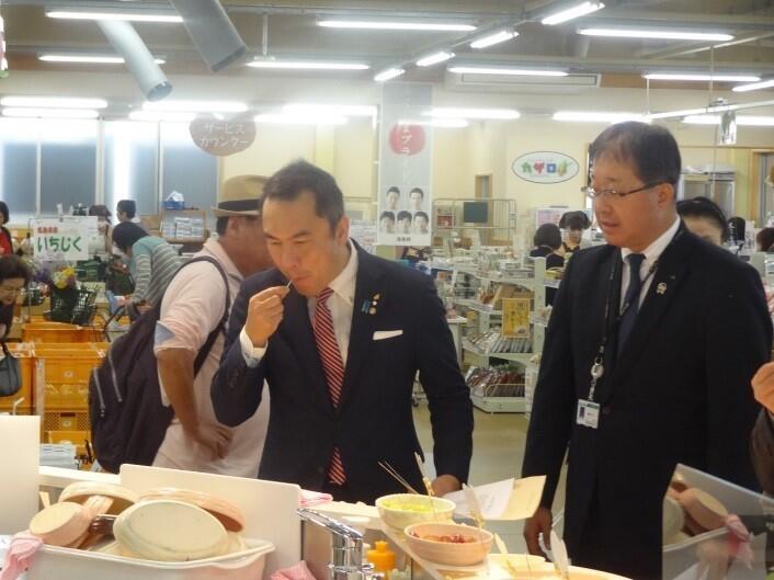 農産物直売所で福島県産の果物を試食する鈴木委員長(中央)